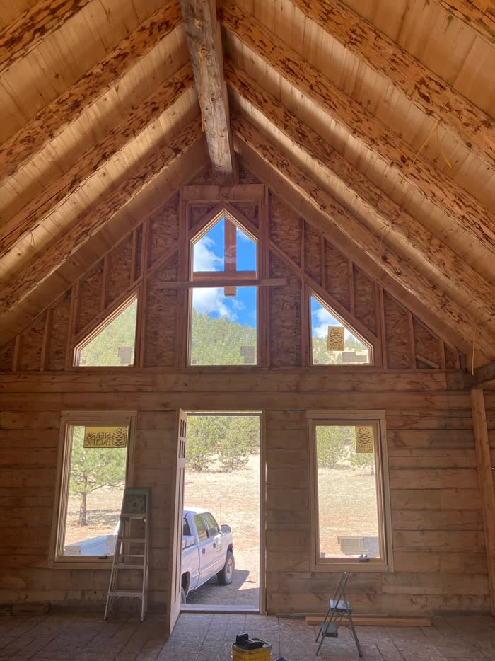Vaulted log ceiling and gable windows looking out on pine forest, under construction
