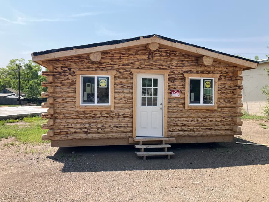 Front of a finished log cabin with two windows and a white door