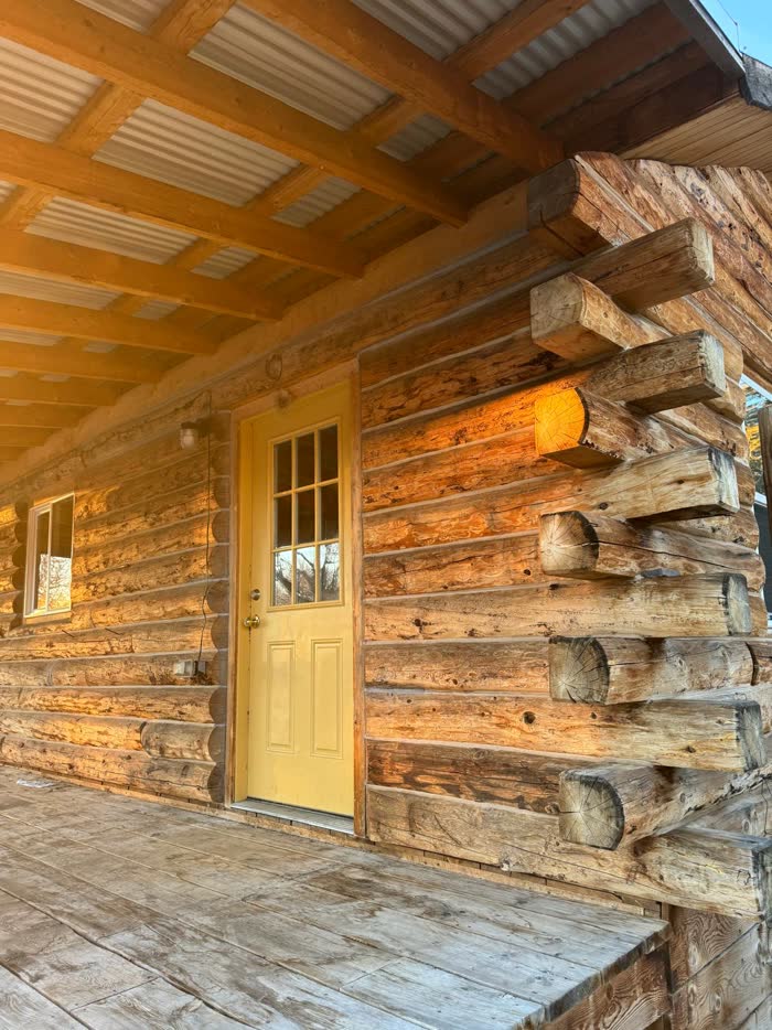 Finished log cabin porch with a yellow front door at sunset